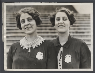 Black and white photograph of Elizabeth and Anna Eliza Smith, identical twins, each wearing a badge, standing outside in front of steps